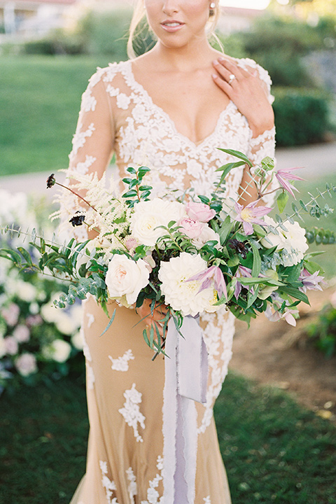 Inn-at-rancho-santa-fe-shoot-bride-holding-flowers-close-up-on-florals-bride-in-a-lace-gown-with-an-illusion-detailing-with-a-nude-underlay-with-her-hair-in-back-in-a-loose-bun