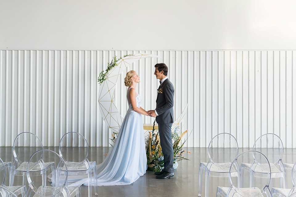 hangar-21-bride-and-groom-at-ceremony-bride-wearing-a-blue-dress-with-lace-details-on-the-bodice-and-flowing-light-blue-material-for-the-skirt-grooom-in-a-charcoal-tuxedo-with-a-matching-charcoal-tie