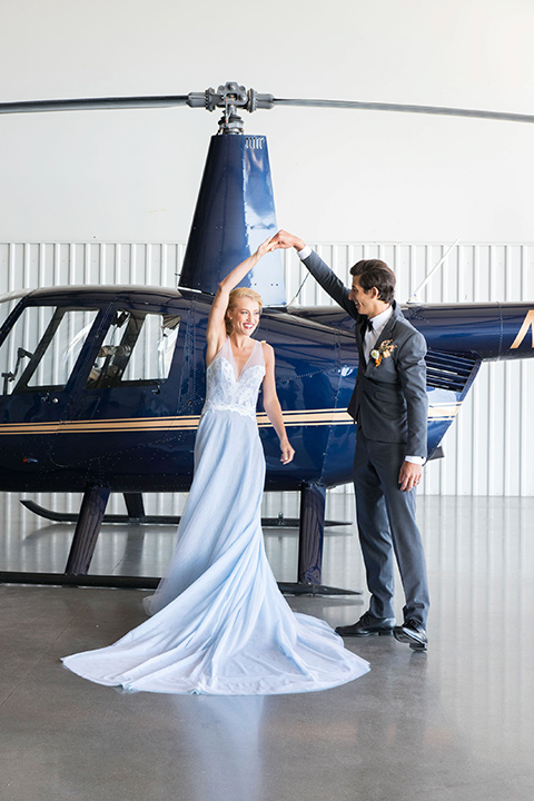 hangar-21-bride-and-groom-dancing-by-helicopter-bride-wearing-a-blue-dress-with-lace-details-on-the-bodice-and-flowing-light-blue-material-for-the-skirt-grooom-in-a-charcoal-tuxedo-with-a-matching-charcoal-tie