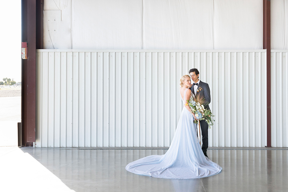 hangar-21-bride-and-groom-in-white-space-bride-wearing-a-blue-dress-with-lace-details-on-the-bodice-and-flowing-light-blue-material-for-the-skirt-grooom-in-a-charcoal-tuxedo-with-a-matching-charcoal-tie