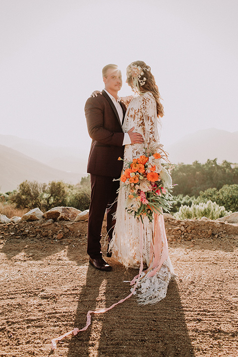 hey-babe-ranch-bride-and-groom-groom-looking-at-camera-bride-looking-at-him-bride-in-a-bohemian-gown-with-lace-and-fringe-detailing-and-hair-in-a-loose-wave-groom-in-a-burgundy-tuxedo-with-black-satin-truim-and-his-tie-undone-for-a-relaxed-look