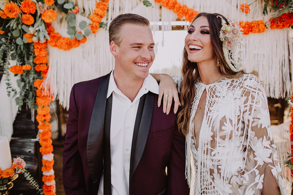 hey-babe-ranch-bride-andgroom-laughing-close-up-bride-in-a-bohemian-gown-with-lace-and-fringe-detailing-and-hair-in-a-loose-wave-groom-in-a-burgundy-tuxedo-with-black-satin-truim-and-his-tie-undone-for-a-relaxed-look