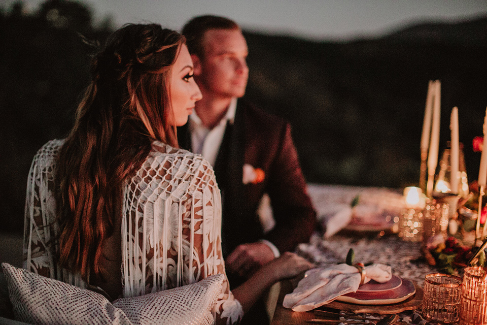 hey-babe-ranch-sunset-couple-picture-bride-in-a-bohemian-gown-with-lace-and-fringe-detailing-and-hair-in-a-loose-wave-groom-in-a-burgundy-tuxedo-with-black-satin-truim-and-his-tie-undone-for-a-relaxed-look