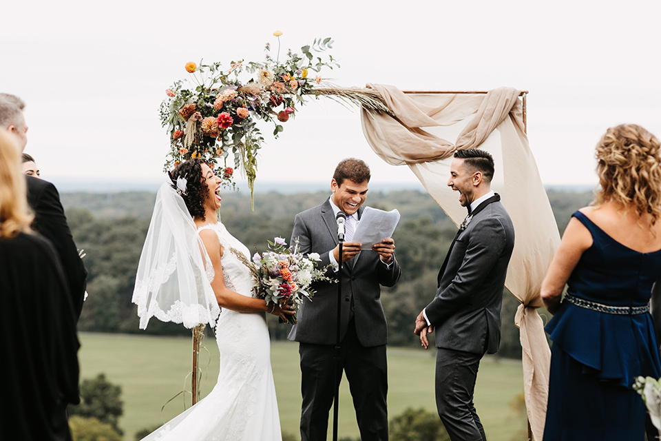 The-Mansion-at-Natirar-bride-and-groom-laughing-at-ceremony-bride-in-a-lace-fitted-dress-with-a-high-neckline-and-hair-up-groom-in-a-grey-tuxedo-with-black-trim-and-a-black-bowtie