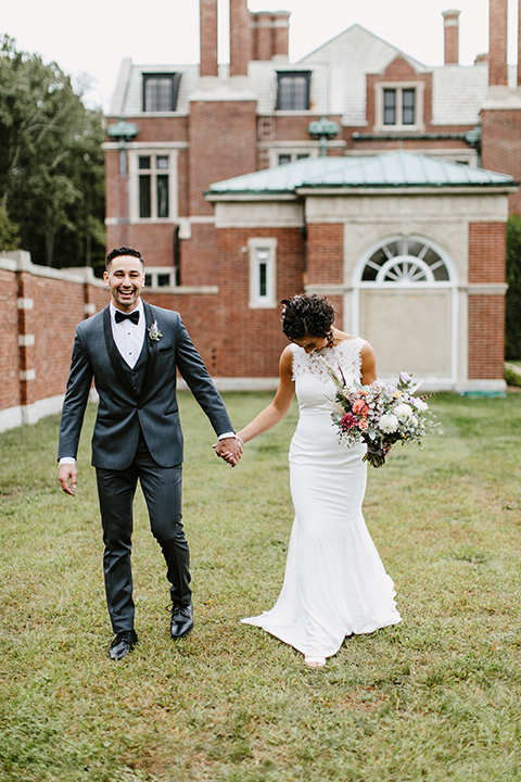 The-Mansion-at-Natirar-bride-and-groom-walking-dress-with-a-high-neckline-and-hair-up-groom-in-a-grey-tuxedo-with-black-trim-and-a-black-bowtie