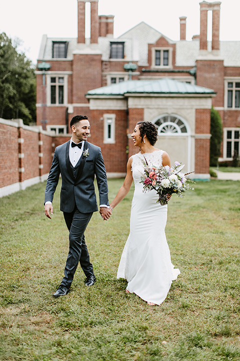 The-Mansion-at-Natirar-bride-and-groom-walking-dress-with-a-high-neckline-and-hair-up-groom-in-a-grey-tuxedo-with-black-trim-and-a-black-bowtie