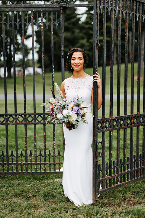 The-Mansion-at-Natirar-bride-by-iron-gate-bride-and-groom-walking-dress-with-a-high-neckline-and-hair-up-groom-in-a-grey-tuxedo-with-black-trim-and-a-black-bowtie