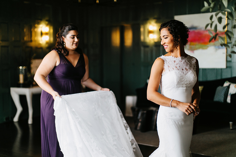 The-Mansion-at-Natirar-bride-putting-on-dress-bride-in-a-lace-fitted-dress-with-a-high-neckline-and-hair-up-groom-in-a-grey-tuxedo-with-black-trim-and-a-black-bowtie