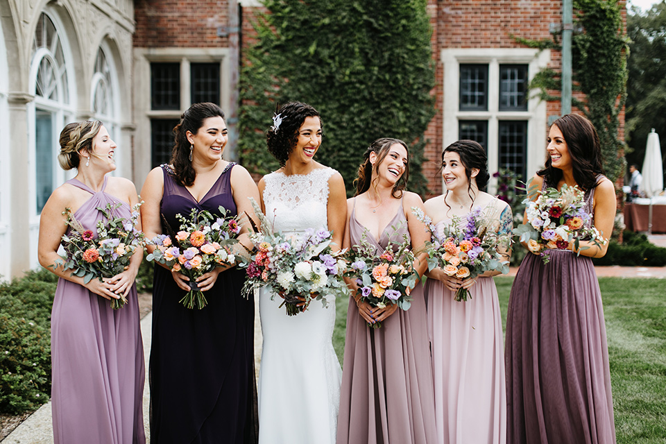 The-Mansion-at-Natirar-bridesmaids-bride-in-a-lace-fitted-dress-with-a-high-neckline-and-hair-up-bridesmaids-in-alternating-purple-dresses