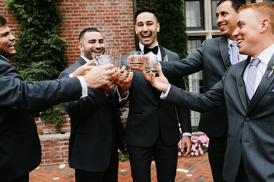 The-Mansion-at-Natirar-groomsmen-cheersing-groom-in-a-grey-tuxedo-with-black-trim-and-a-black-bowtie-groomsmen-in-grey-tuxedos-with-purple-ties