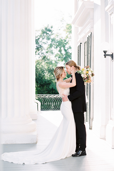 Taylor-Grady-House-shoot-bride-and-groom-facing-each-other-bride-touching-grooms-face-bride-in-a-fit-and-flar-silk-gown-with-an-open-back-detail-and-hair-in-a-loose-bun-groom-wearing-a-black-notch-lapel-tuxedo-with-a-black-bowtie-and-hair-in-a-bun