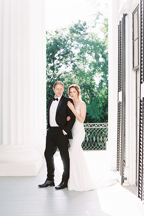 Taylor-Grady-House-shoot-bride-and-groom-standing-bride-behind-groom-grooms-hands-in-his-pockets-bride-in-a-fit-and-flar-silk-gown-with-an-open-back-detail-and-hair-in-a-loose-bun-groom-wearing-a-black-notch-lapel-tuxedo-with-a-black-bowtie-and-hair-in-a-bun