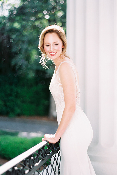 Taylor-Grady-House-shoot-bride-leaning-on-railing-bride-in-a-fit-and-flar-silk-gown-with-an-open-back-detail-and-hair-in-a-loose-bun