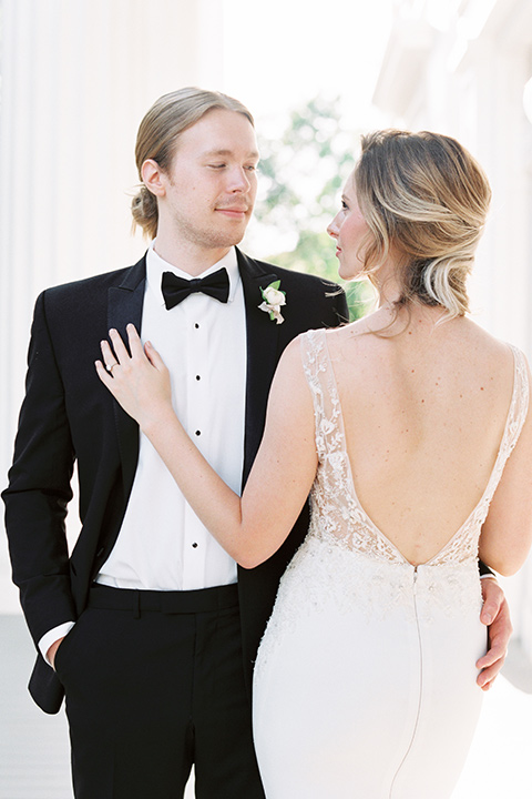 Taylor-Grady-House-shoot-close-up-on-bride-and-groom-groom-facing-camera-bride-back-towards-camera-bride-in-a-fit-and-flar-silk-gown-with-an-open-back-detail-and-hair-in-a-loose-bun-groom-wearing-a-black-notch-lapel-tuxedo-with-a-black-bowtie-and-hair-in-a-bun