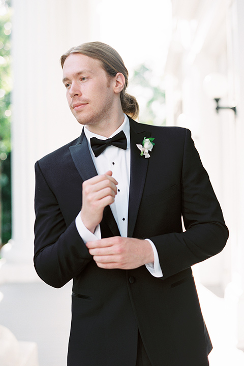 Taylor-Grady-House-shoot-close-up-on-groom-groom-wearing-a-black-notch-lapel-tuxedo-with-a-black-bowtie-and-hair-in-a-bun