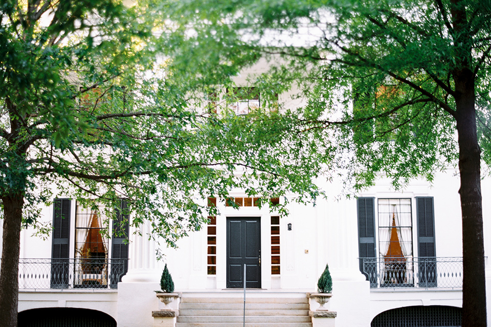 Taylor-Grady-House-shoot-outside-of-venue-green-lush-trees-in-the-foreground-the-white-house-in-the-background-with-white-bricks-and-black-trimming