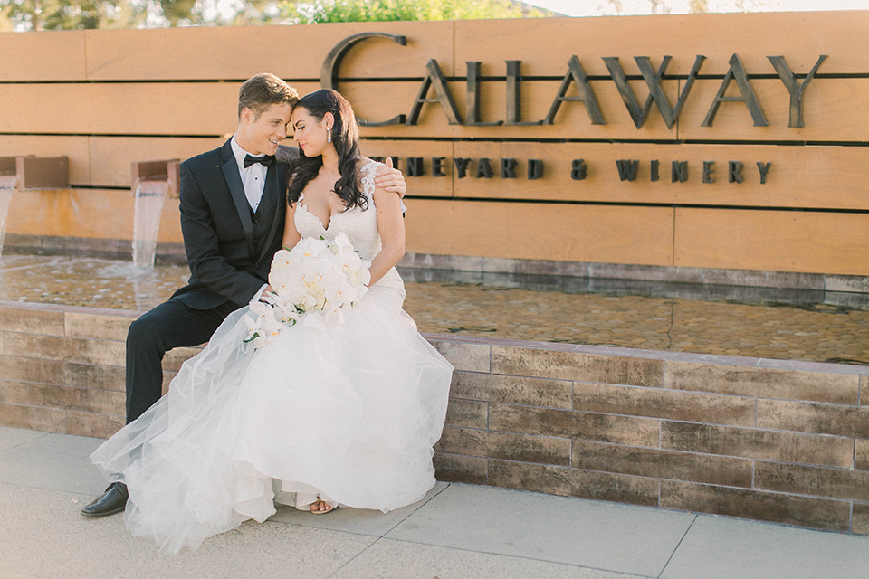callaway-winery-shoot-bride-and-groom-by-the-callaway-winery-sign-bride-wearing-a-fitted-dress-with-straps-and-tulle-and-lace-detailing-while-the-groom-wore-a-traditional-black-tuxedo-with a-black-bowtie