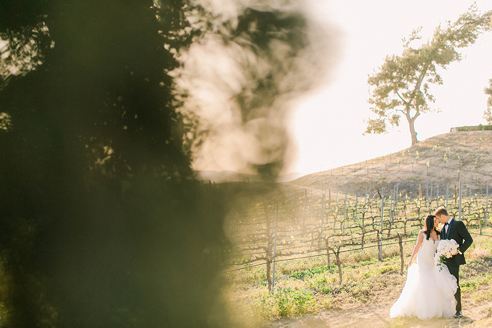 callaway-winery-shoot-bride-and-groom-in-vinyard-far-away-shot-bride-wearing-a-fitted-dress-with-straps-and-tulle-and-lace-detailing-while-the-groom-wore-a-traditional-black-tuxedo-with a-black-bowtie