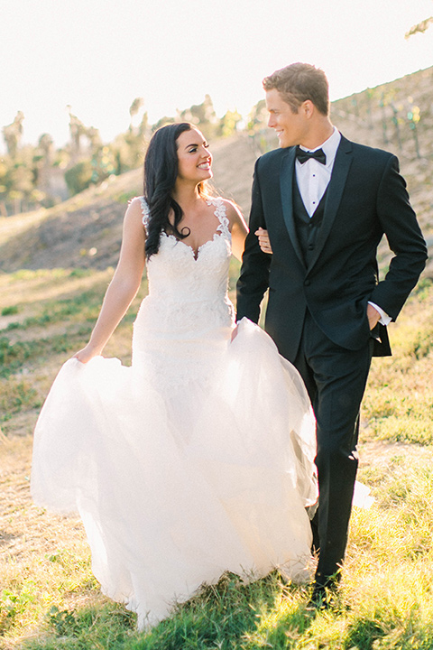 callaway-winery-shoot-bride-and-groom-smiling-and-holding-hands-bride-wearing-a-fitted-dress-with-straps-and-tulle-and-lace-detailing-while-the-groom-wore-a-traditional-black-tuxedo-with a-black-bowtie