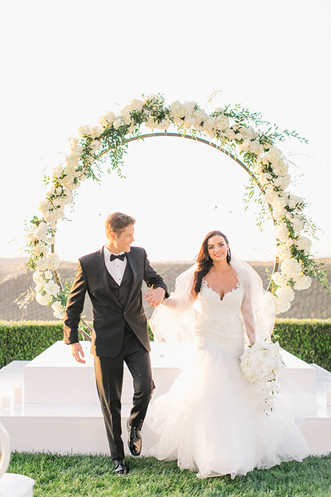 callaway-winery-shoot-bride-and-groom-walking-away-from-ceremony-part-two-bride-wearing-a-fitted-dress-with-straps-and-tulle-and-lace-detailing-while-the-groom-wore-a-traditional-black-tuxedo-with a-black-bowtie