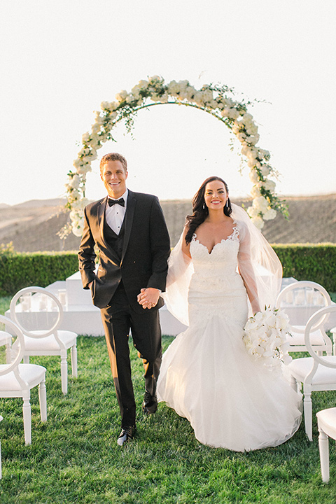 callaway-winery-shoot-bride-and-groom-walking-away-from-ceremony-bride-wearing-a-fitted-dress-with-straps-and-tulle-and-lace-detailing-while-the-groom-wore-a-traditional-black-tuxedo-with a-black-bowtie