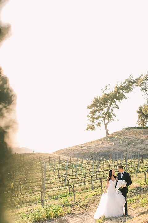 callaway-winery-shoot-bride-and-groom-walking-in-the-winery-looking-at-each-other-bride-wearing-a-fitted-dress-with-straps-and-tulle-and-lace-detailing-while-the-groom-wore-a-traditional-black-tuxedo-with a-black-bowtie