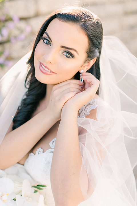 callaway-winery-shoot-bride-putting-on-her-earrings-bride-wearing-a-fitted-dress-with-straps-and-tulle-and-lace-detailing