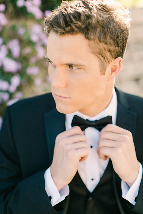 callaway-winery-shoot-close-up-of-groom-holding-bow-tie-groom-wearing-a-traditional-tuxedo-with-a-black-bowtie-and-black-shoes