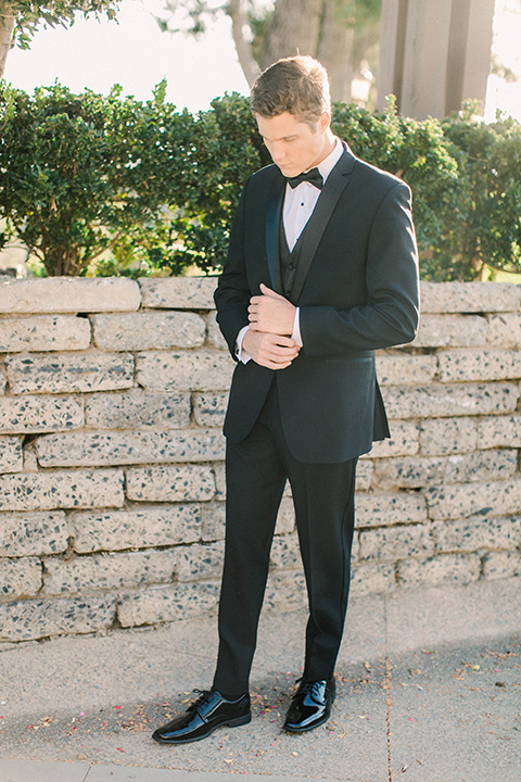callaway-winery-shoot-groom-standing-looking-down-groom-wearing-a-traditional-tuxedo-with-a-black-bowtie-and-black-shoes