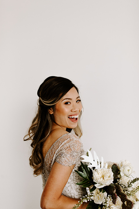 huntington-bay-club-shoot-bride-alone-looking-over-her-shoulder-bride-wearing-a-flowing-dress-with-a-beaded-bodice-and-sleeves