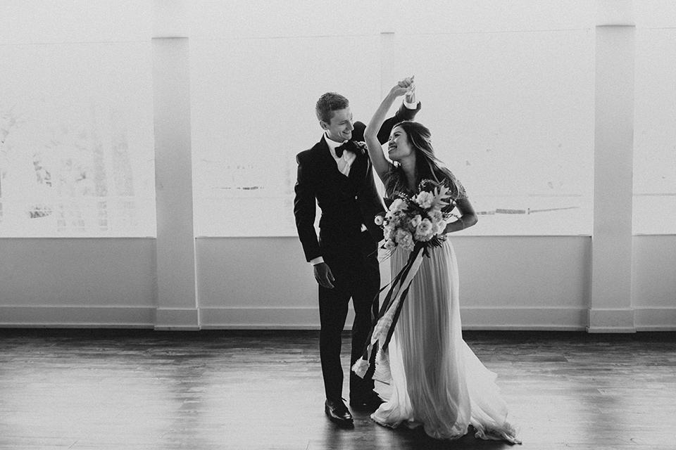 huntington-bay-club-shoot-bride-and-groom-dancing-bride-wearing-a-flowing-gown-with-a-beaded-bodice-and-ca-sleeves-groom-wearing-a-black-suit-with-a-green-velvet-bow-tie