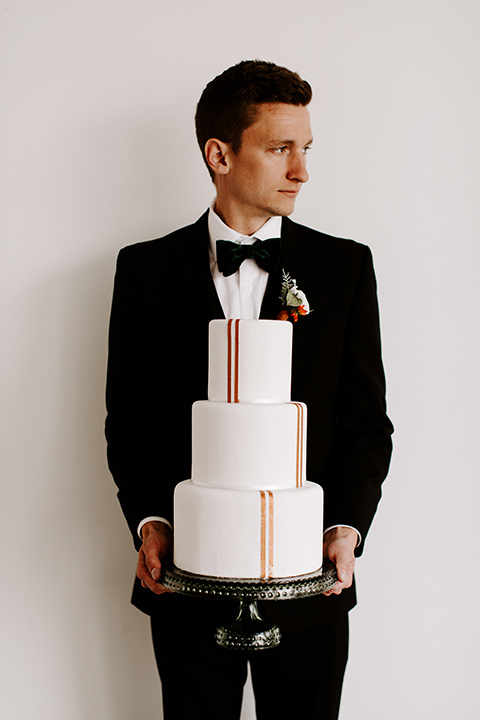 huntington-bay-club-shoot-groom-holding-cake-groom-wearing-a-black-suit-with-a-green-velvet-bow-tie