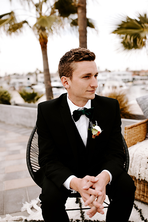 huntington-bay-club-shoot-groom-siting-groom-wearing-a-black-suit-with-a-green-velvet-bow-tie