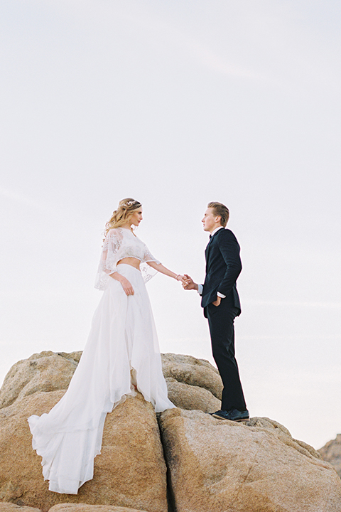 Joshua-tree-wedding-shoot-at-the-ruin-venue-bride-and-groom-standing-on-rocks-holding-hands