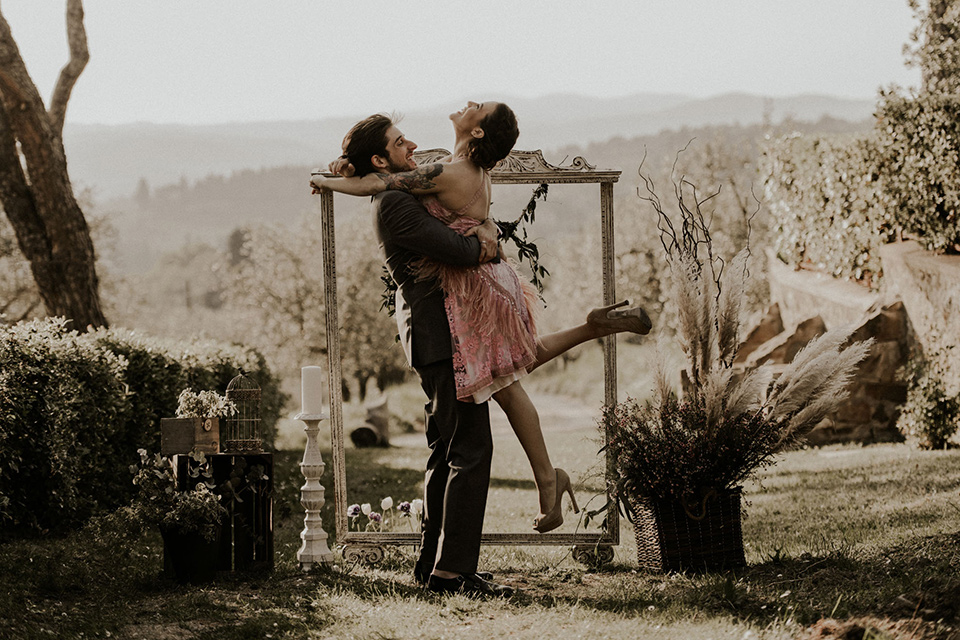 la-dolce-vita-bride-and-groom-laughing-at-ceremony-bride-in-a-pink-colored-dress-with-lace-detailing-groom-in-grey-suit-pants-and-vest