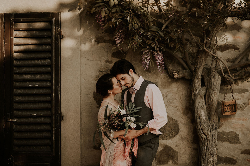 la-dolce-vita-bride-and-groom-under-the-tree-bride-in-a-pink-colored-dress-with-lace-detailing-groom-in-grey-suit-pants-and-vest