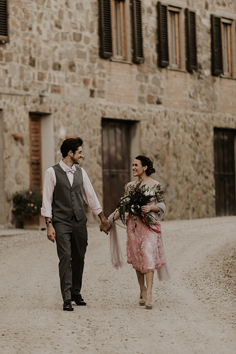 la-dolce-vita-shoot-bride-and-groom-on-the-cobblestone-path-bride-wearing-a-pink-colored-dress-with-lace-detailing-groom-in-grey-pants-and-a-grey-vest