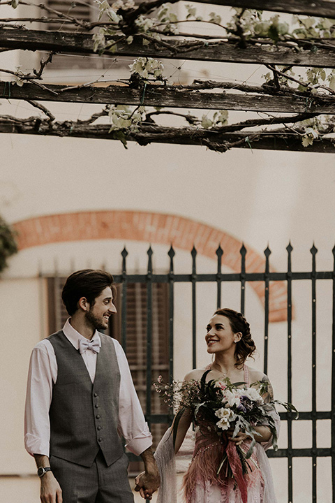 la-dolce-vita-shoot-bride-and-groom-walking-bride-wearing-a-pink-colored-dress-with-lace-detailing-groom-in-grey-pants-and-a-grey-vest