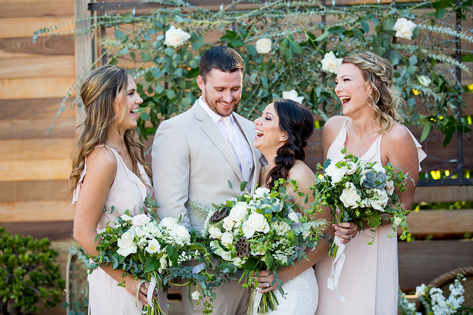 lot-8-bridal-party-laughing-bride-wearing-a-strapless-white-gown-with-lave-groom-in-a-light-grey-suit-with-silver-tie-braideamaids-in-blush-dresses-holding-floral-bouquets-and-all-laughing