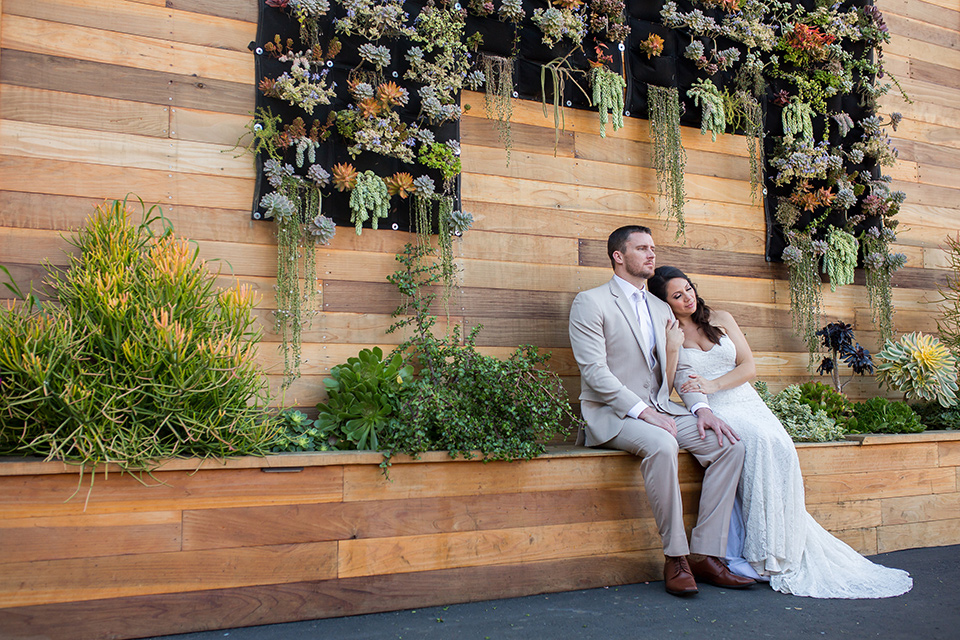 lot-8-bride-and-groom-with-succulent-wall-bride-wearing-a-white-strapless-bridal-gown-with-lace-embellishments-hair-in-a-loose-braid-groom-wearing-a-light-grey-suit-with-a-silver-tie-and-light-brown-shoes