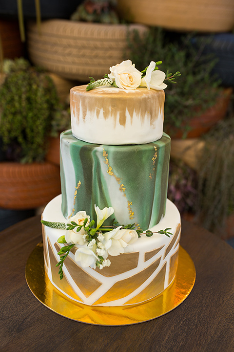 lot-8-cake-three-teirs-gold-and-green-with-geometirc-pattern-on-the-bottom-layer-and-white-flowers-adorning-the-top