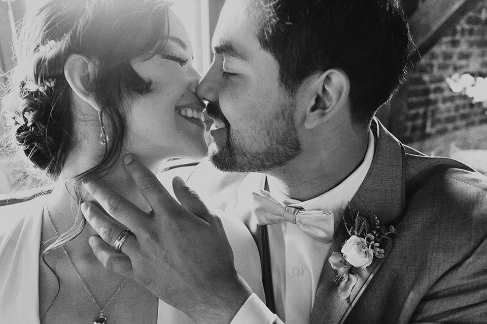 The-mitten-building-shoot-black-andwhite-picture-of-bride-and-groom-about-to-kiss-bride-in-a-retro-inspired-gown-with-hair-in-a-bun-and-fingerwaves-groom-in-a-light-grey-suit-with-a-blue-bow-tie-and-brown-shoes