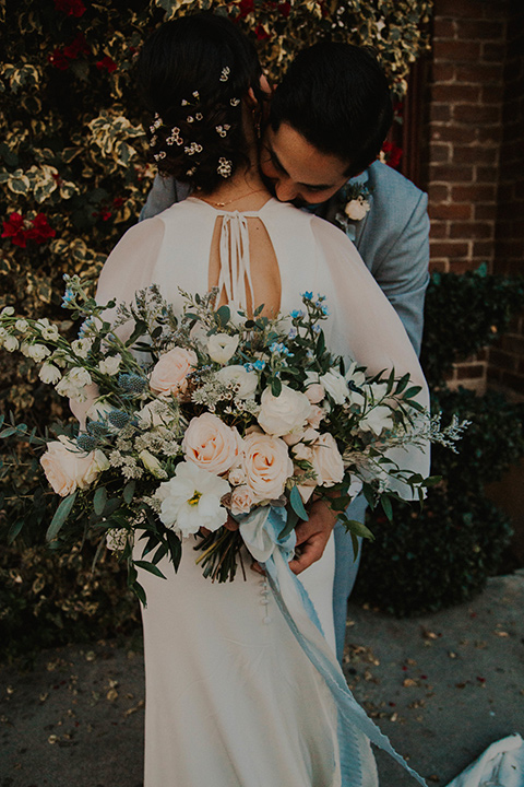 The-mitten-building-shoot-bride-and-groom-huggin-back-turned-to-camera-bride-in-a-retro-inspired-gown-with-hair-in-a-bun-and-fingerwaves-groom-in-a-light-grey-suit-with-a-blue-bow-tie-and-brown-shoes