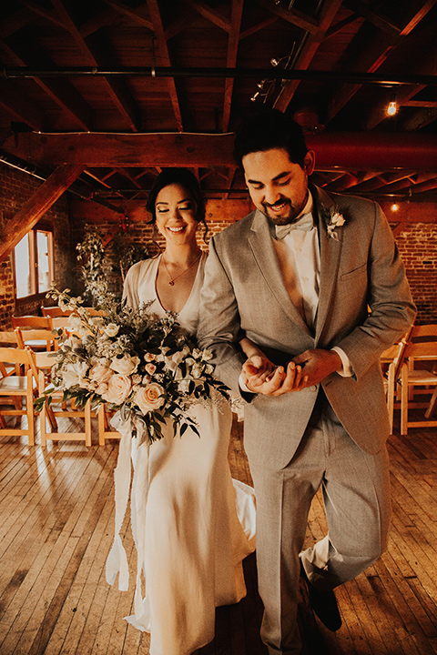 The-mitten-building-shoot-bride-and-groom-walking-away-from-ceremony-bride-in-a-retro-inspired-gown-with-hair-in-a-bun-and-fingerwaves-groom-in-a-light-grey-suit-with-a-blue-bow-tie-and-brown-shoes