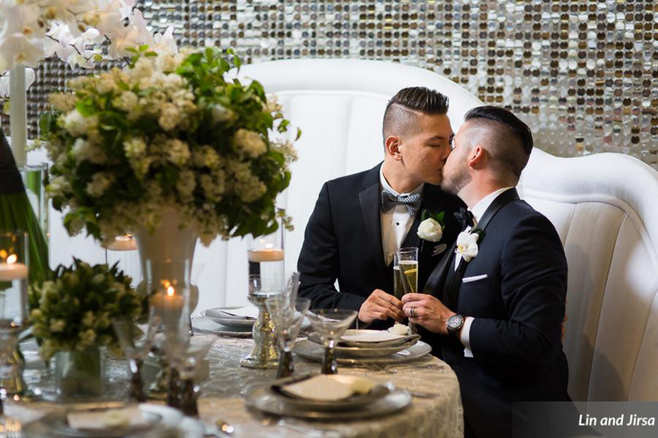 Laguna-beach-outdoor-wedding-same-sex-grooms-sitting-at-table-kissing