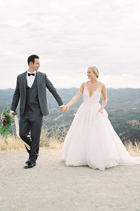 mountain-elopement-shoot-bride-and-groom-walking-Bride-in-a-tulle-ball-gown-with-an-illusion-bodice-and-lace-detailing-groom-at-sweetheart-table-groom-in-a-grey-tuxedo-with-a-black-bowtie