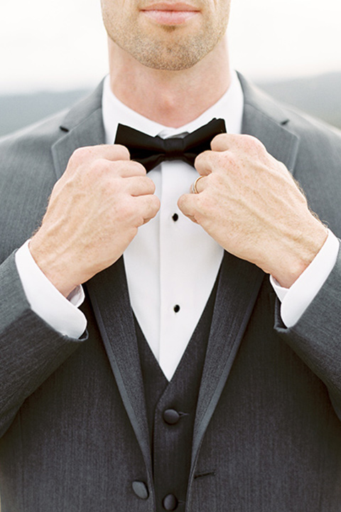 mountain-elopement-shoot-close-up-on-groom-Bride-in-a-tulle-ball-gown-with-an-illusion-bodice-and-lace-detailing-groom-at-sweetheart-table-groom-in-a-grey-tuxedo-with-a-black-bowtie