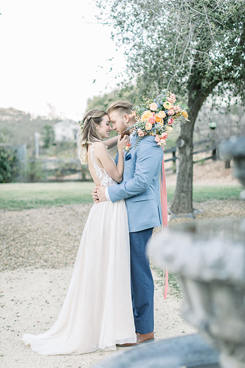 alice-in-wonderland-shoot-bride-and-groom-at-reception-bride-in-a-white-gown-with-lace-detailing-and-a-flowing-skirt-groom-in-a-light-blue-coat-with-dark-blue-pants-and-a-floral-long-tie