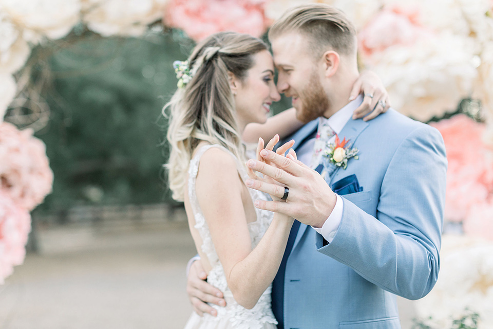 alice-in-wonderland-shoot-bride-and-groom-dancing-bride-in-a-white-gown-with-a-flowing-skirt-and-low-back-detail-groom-in-a-light-blue-coat-with-dark-blue-pants-and-vest-and-a-floral-long-tie