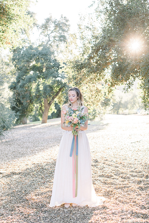 alice-in-wonderland-shoot-bride-holding-flowers-in-a-white-gown-with-lace-detailing-and-a-flowing-skirt